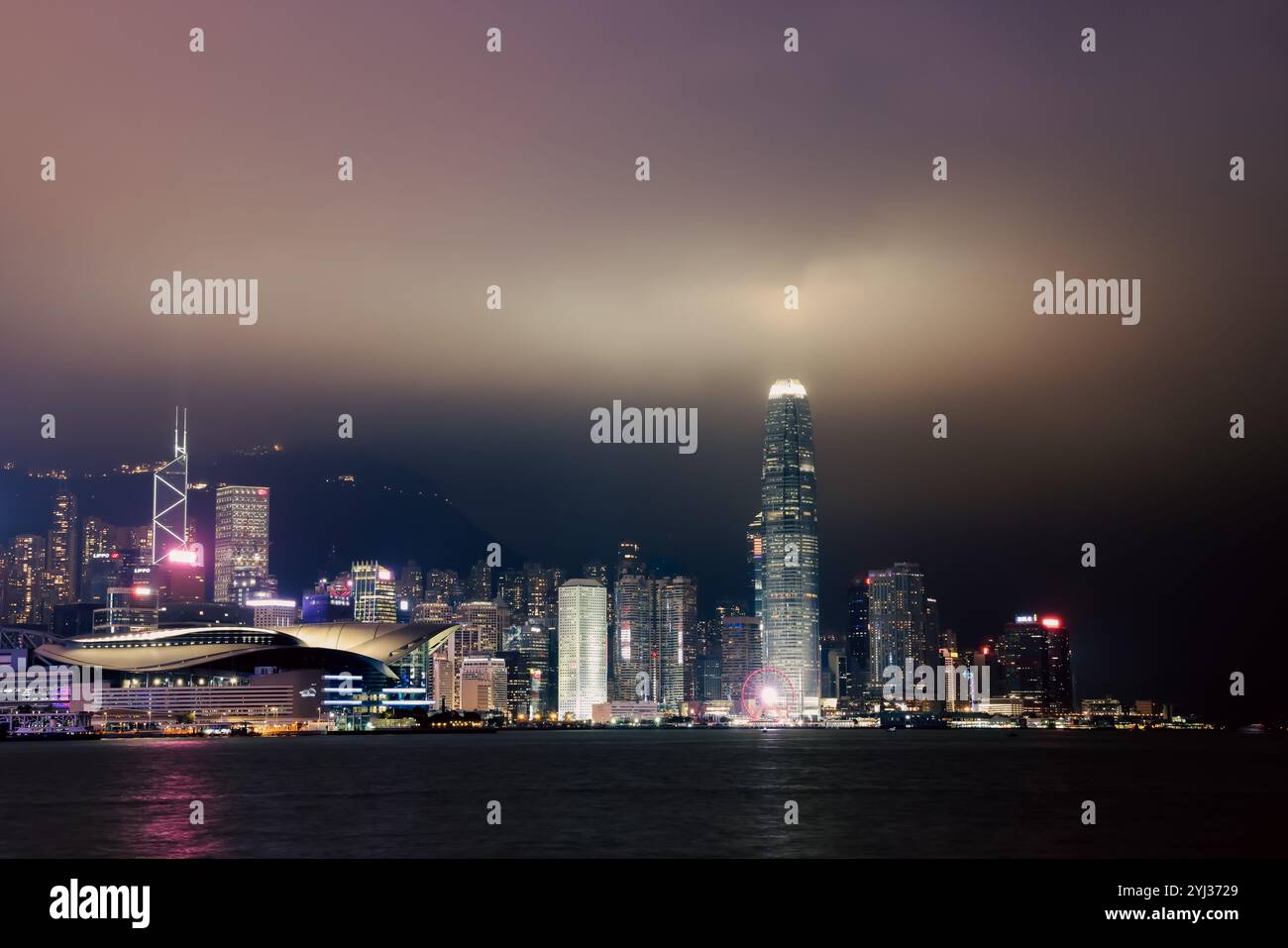 Ein lebhafter nächtlicher Blick auf die Skyline von Hongkong, der brillante Lichter vor einem bewölkten Himmel reflektiert. Stockfoto