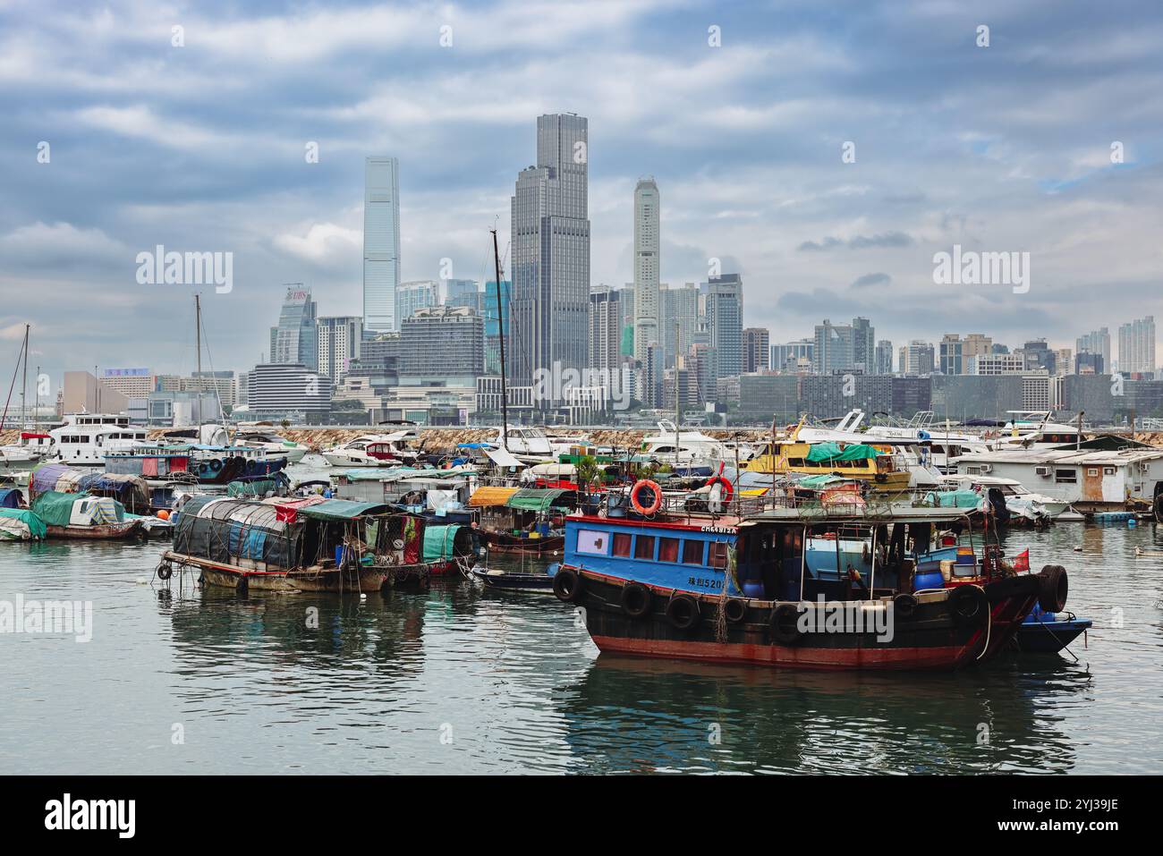 Ein lebhafter Hafen voller traditioneller Holzboote vor der Kulisse der beeindruckenden Skyline und des bewölkten Himmels von Hongkong. Stockfoto