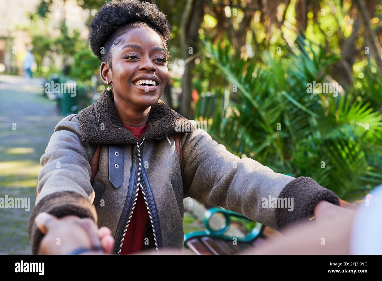 Fröhliche Frau, die an einem sonnigen Tag im Grünen Park Hände hält Stockfoto