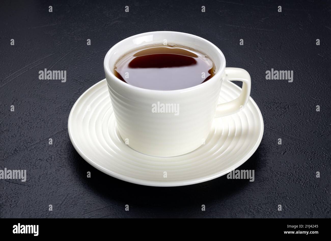 Eine Tasse schwarzen Tee in einem weißen Keramikbecher auf schwarzem Hintergrund. Stockfoto