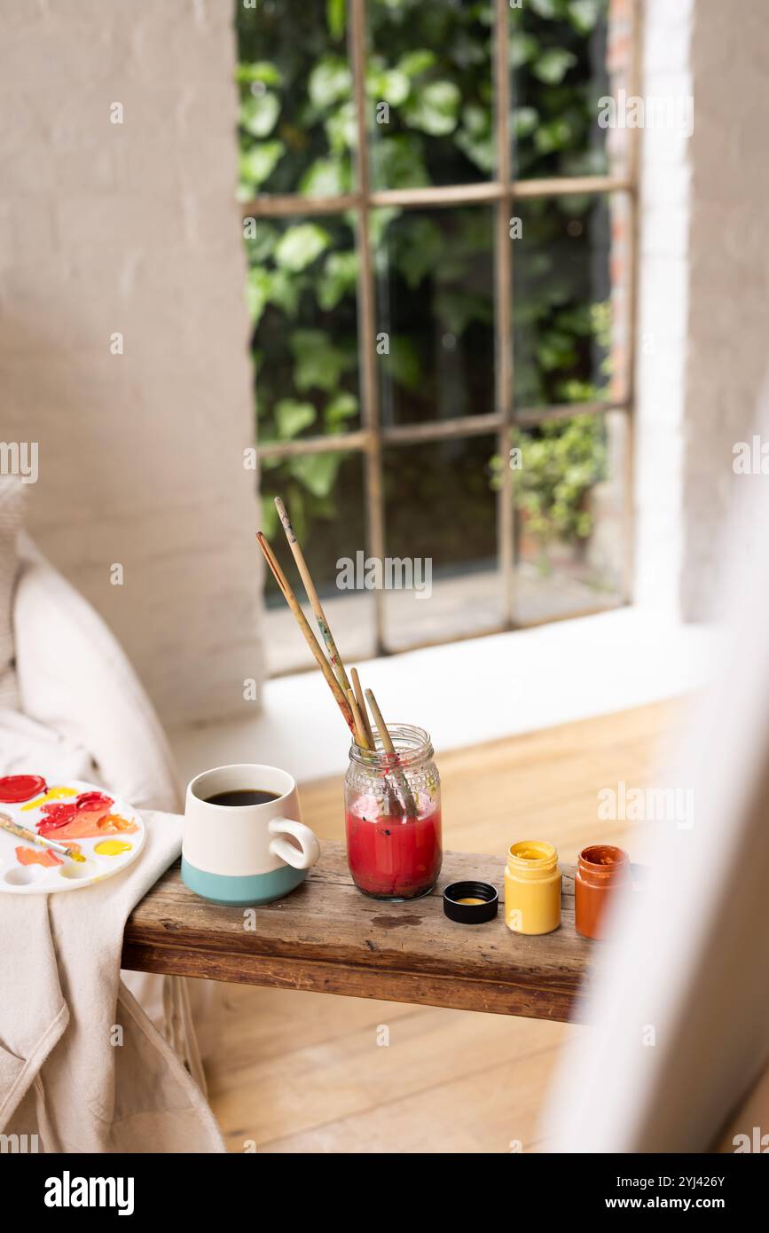 Kunstzubehör und Kaffee auf Holztisch in der Nähe des Fensters schaffen eine gemütliche Atmosphäre, zu Hause Stockfoto