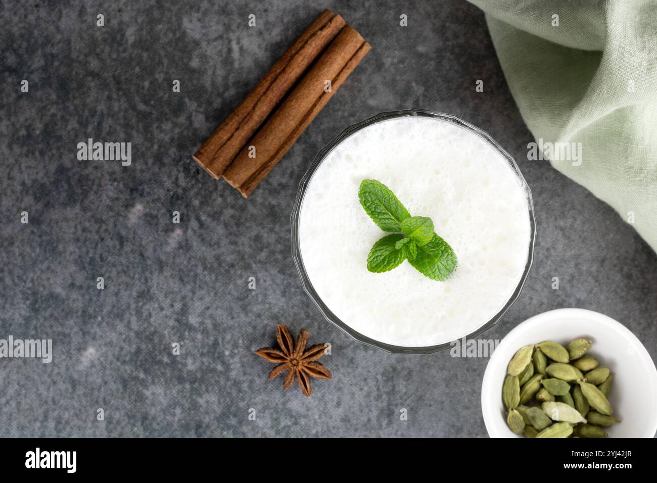 Traditionelles indisches Joghurtgetränk mit Gewürzen: Kardamom, Zimtstab und Minze auf grauem Hintergrund. Draufsicht, Kopierraum. Stockfoto