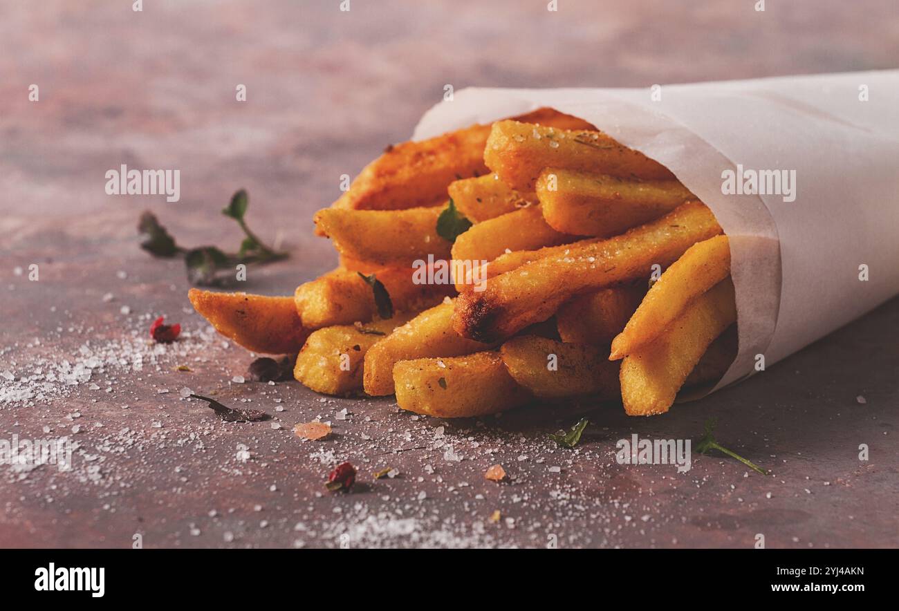 Frittierte Pommes frites, in einer Papiertüte, auf abstraktem Hintergrund, keine Leute, rustikal Stockfoto