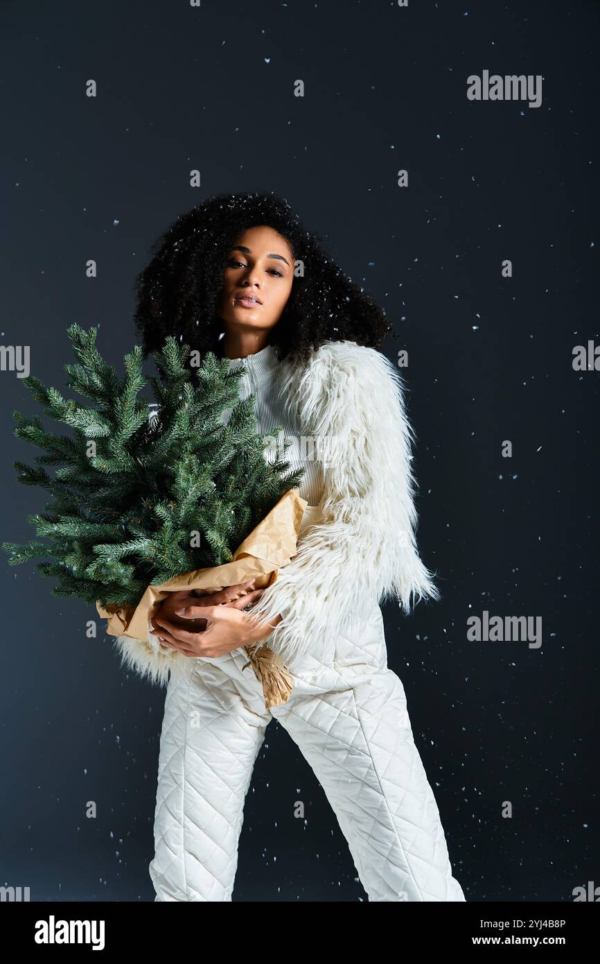 Eine modische Afroamerikanerin hält einen kleinen immergrünen Baum, während sie für winterliche Eleganz gekleidet ist. Stockfoto