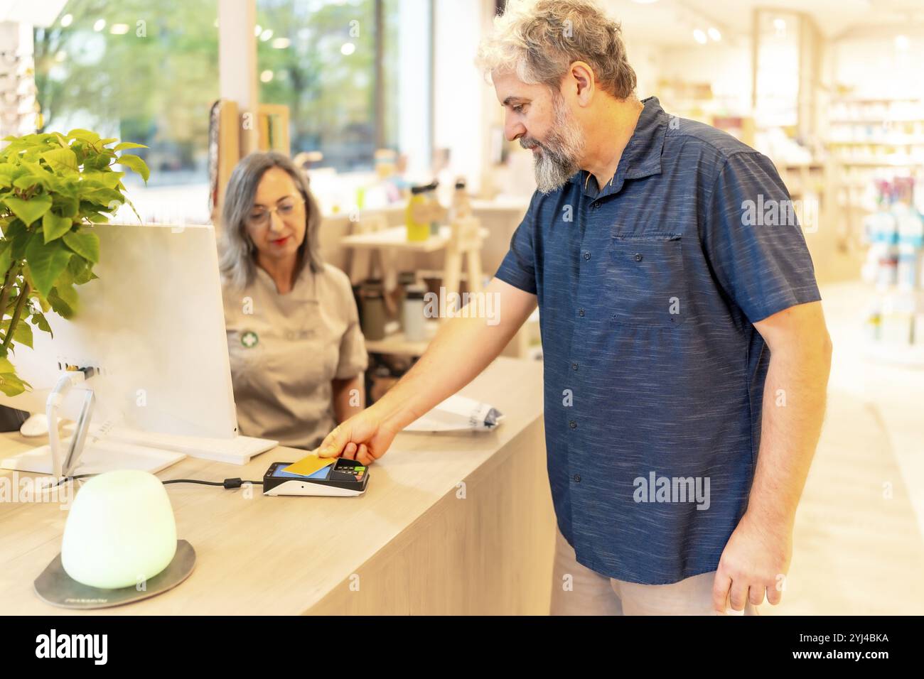 Reifer kaukasier, der am Tresen steht und mit Kreditkarte in einem Apothekenladen bezahlt Stockfoto