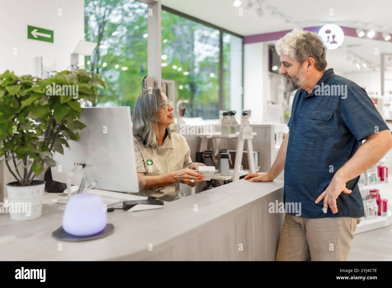 Weibliche, reife Apothekerin, die sich um einen Kunden in einem Geschäft kümmert Stockfoto