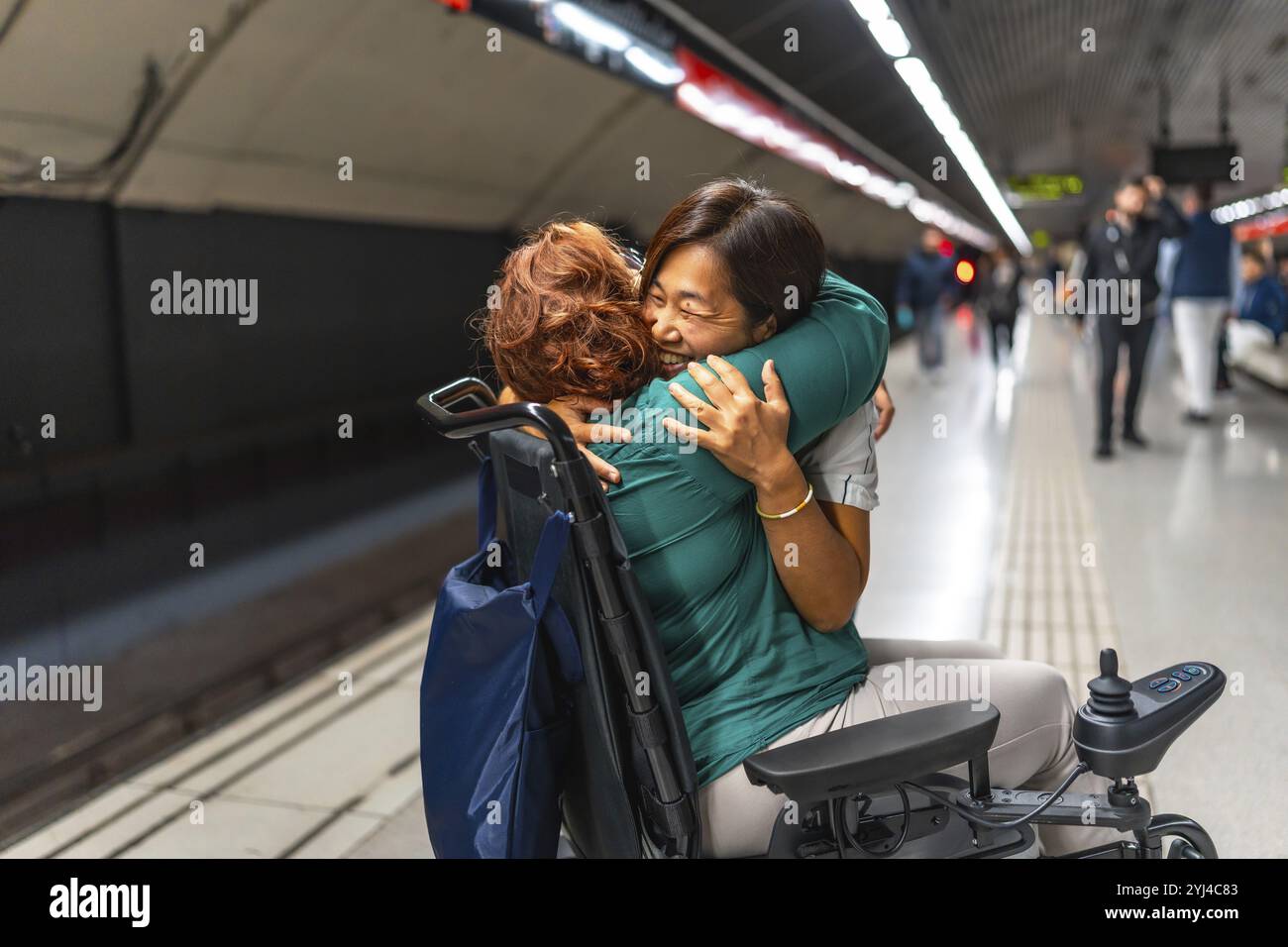 Glückliche behinderte Frau und chinesische Betreuerin, die sich auf der U-Bahn-Plattform der Stadt umarmen Stockfoto