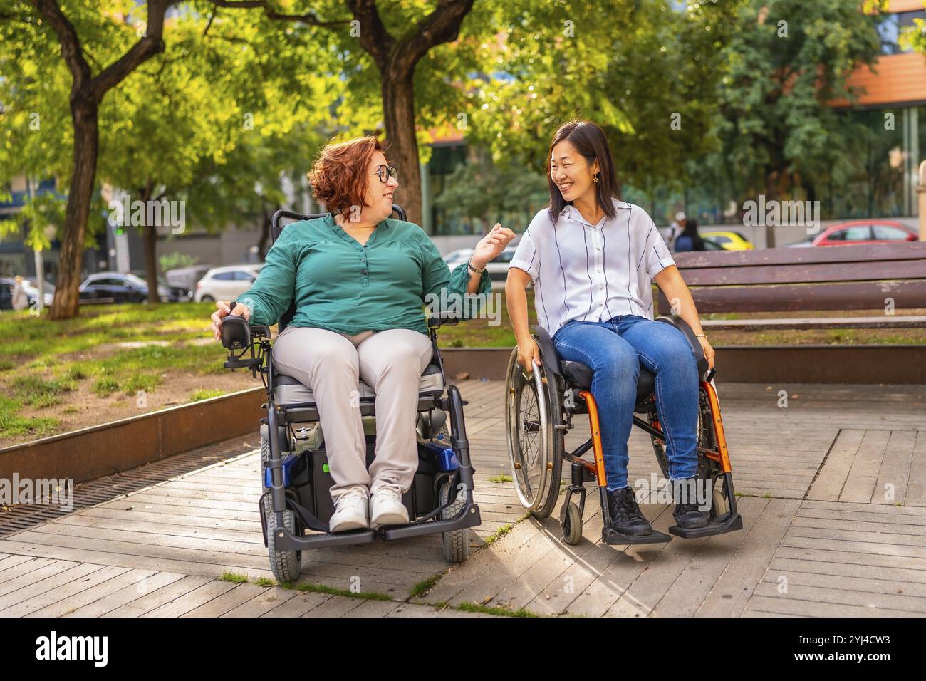 Glückliche Rollstuhlfahrerinnen, multiethnische Freunde, verbringen gerne Zeit zusammen in einem öffentlichen Park Stockfoto