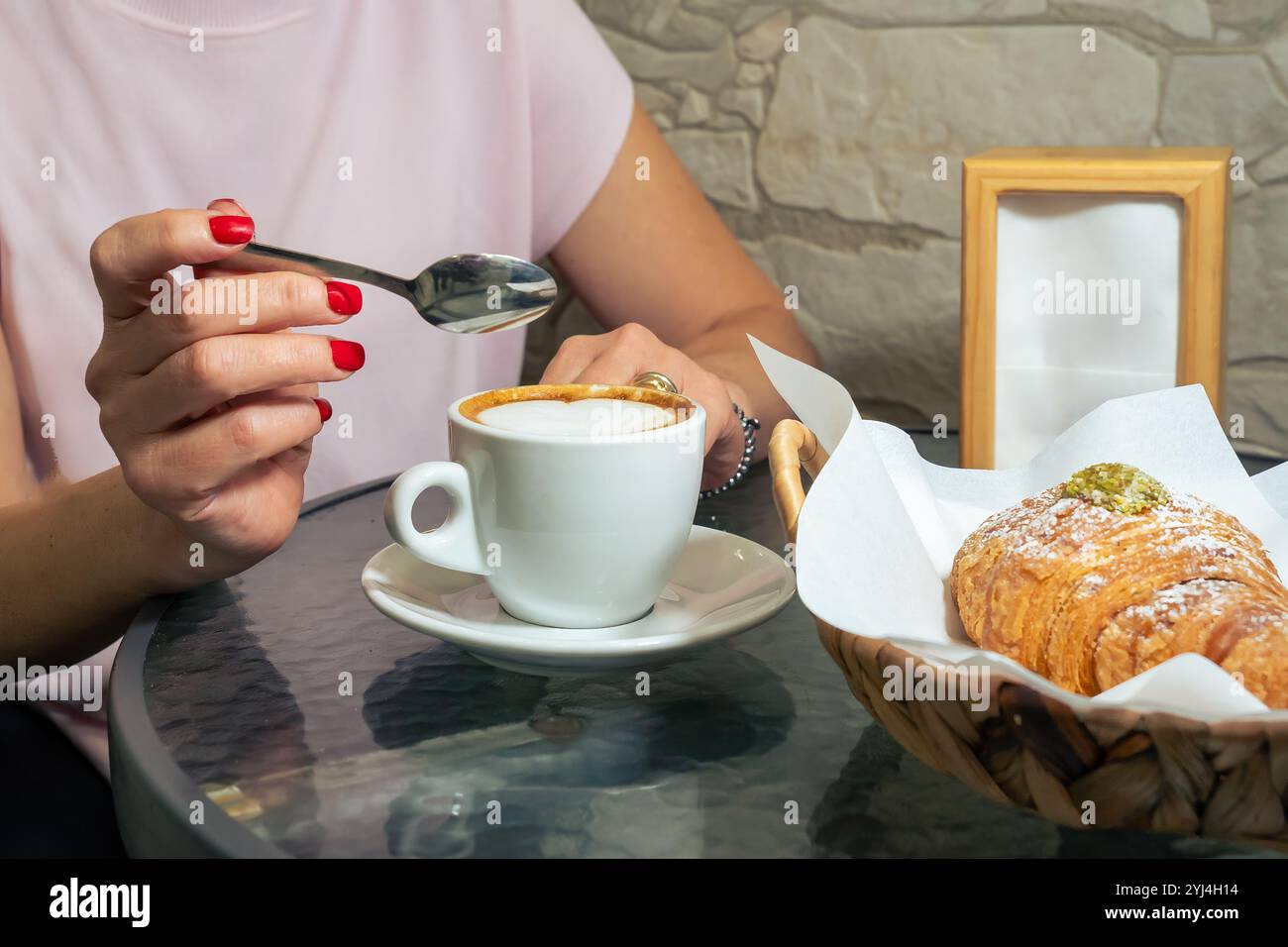 Frau mit roter Maniküre genießt italienisches Frühstück mit Cappuccino und Croissant am Morgen Café Lifestyle Moment Stockfoto