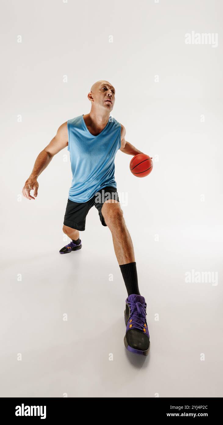 Basketballspieler mit Tanktop und Turnshorts dribbelt Basketball und bereitet sich auf das Schießen vor grauem Studiohintergrund vor. Stockfoto