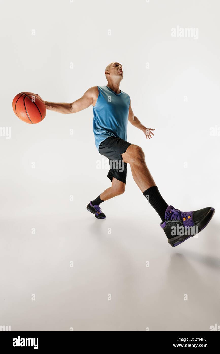 Ein kleiner Schuss eines männlichen Basketballspielers im sportlichen Outfit dribbelt und sieht konzentriert aus, während er sich auf den Schuss vor grauem Studiohintergrund vorbereitet. Stockfoto