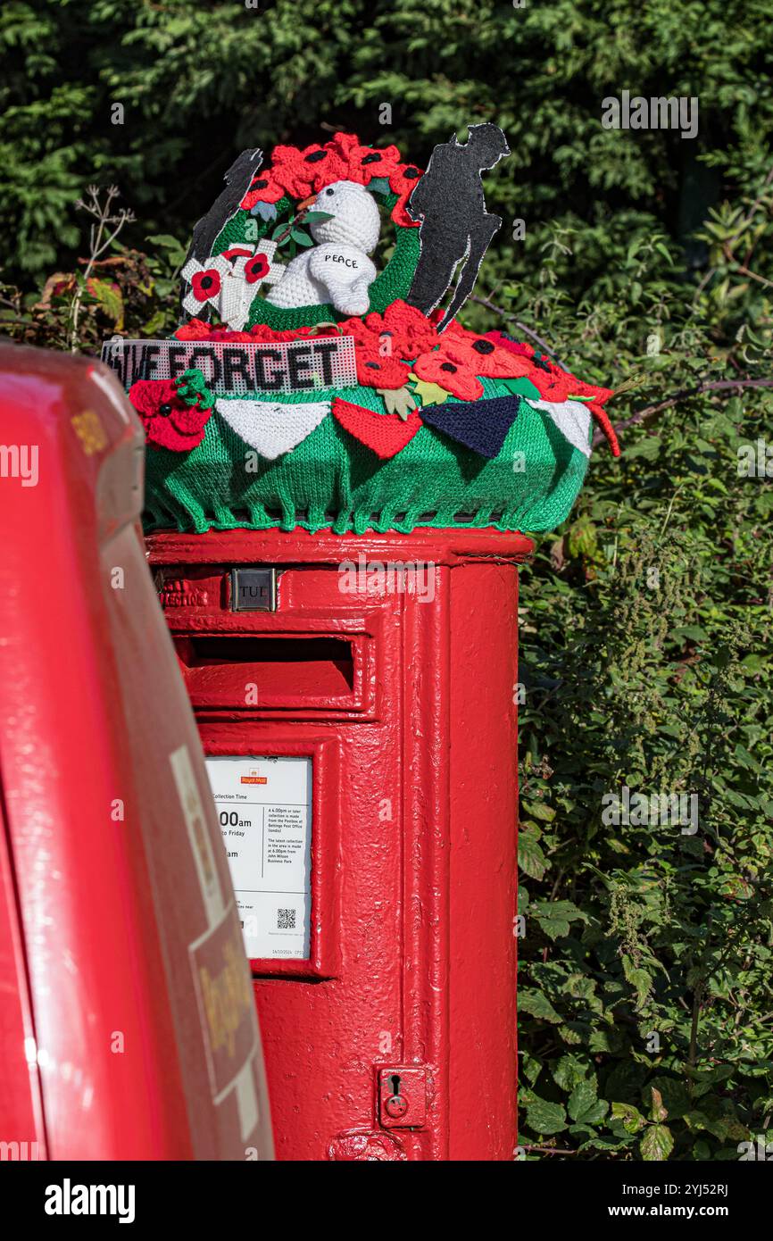 „Lest We Forget“-Briefkasten-Topper auf einem traditionellen roten Postfach mit einer grünen Hecke dahinter und einem Postwagen im Vorfeld Stockfoto