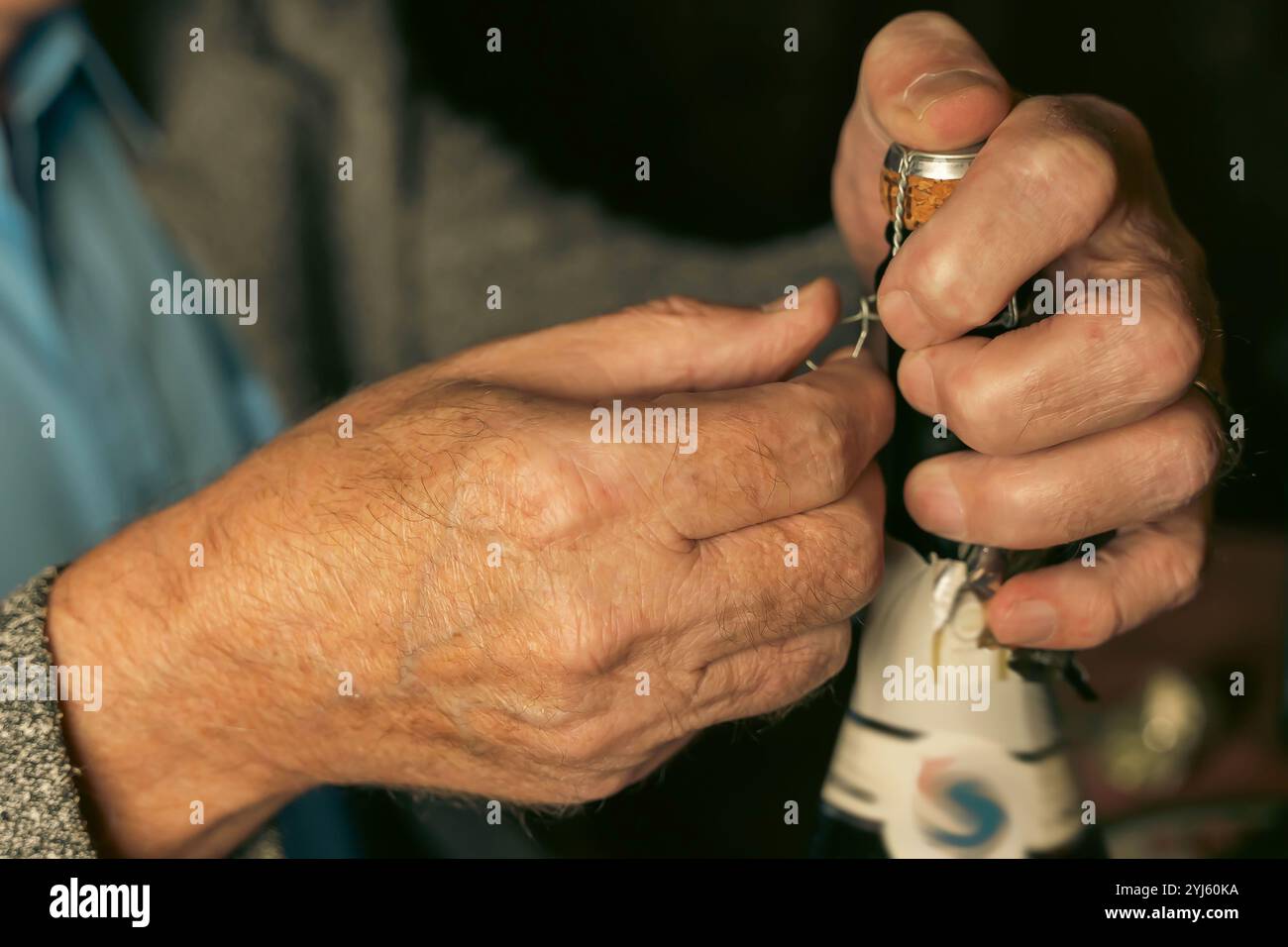 Nahaufnahme der Hände des älteren Mannes vorsichtig den Drahtkäfig von der Sektflasche lösen und sich auf die Feier vorbereiten Stockfoto