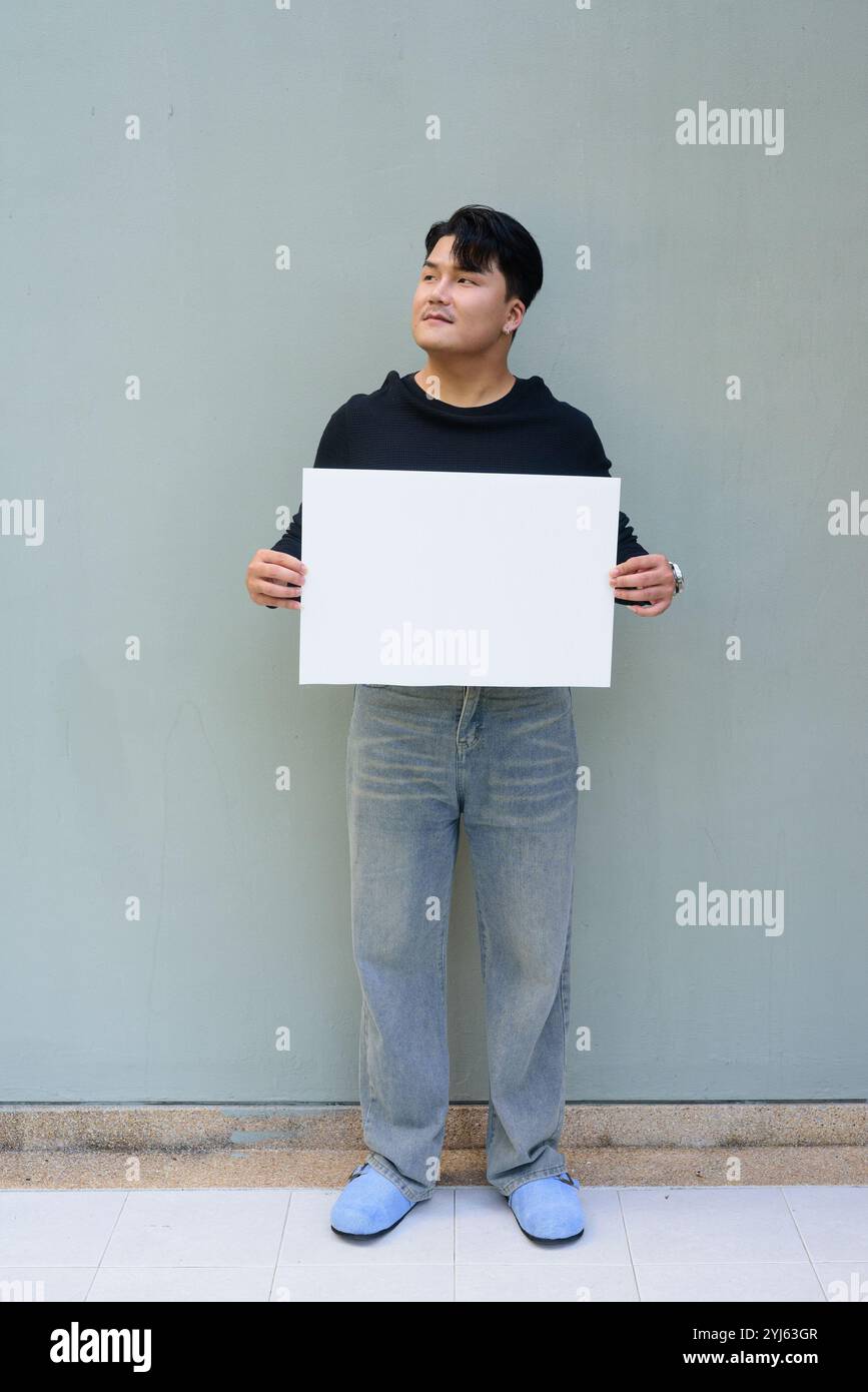 Porträt des hübschen jungen asiatischen Mannes vor einem einfachen Hintergrund im Freien Stockfoto