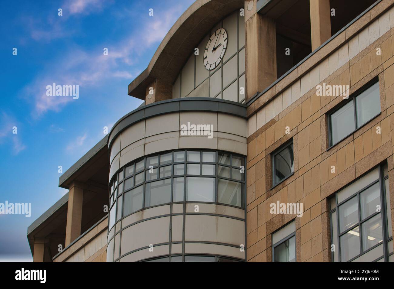 Ein Gebäude mit einem geschwungenen Abschnitt und mehreren Fenstern, einschließlich einer großen Uhr, vor einem blauen Himmel mit schroffen Wolken. Stockfoto