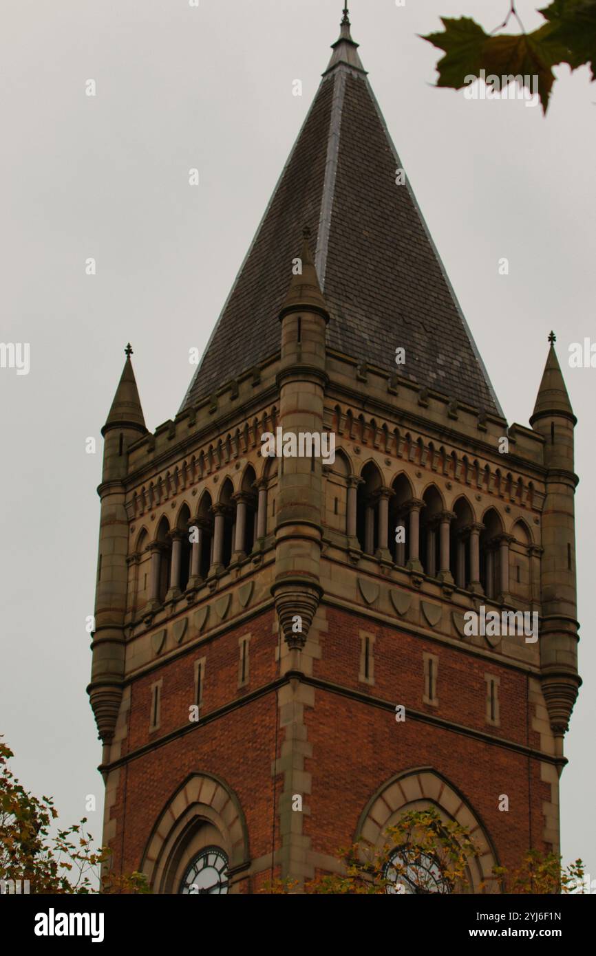 Aus nächster Nähe ein hoher, gemauerter Turm mit einem schrägen Schieferdach und einem spitzen Turm. Der Turm ist mit Bogenfenstern und dekorativen Elementen geschmückt Stockfoto