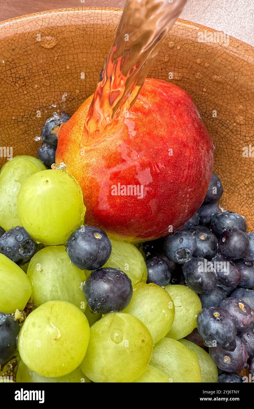 Nahaufnahme von frischem Obst, Heidelbeeren, Pfirsich und Trauben in einer Schüssel unter fließendem Wasser, während die Früchte gewaschen werden. Stockfoto