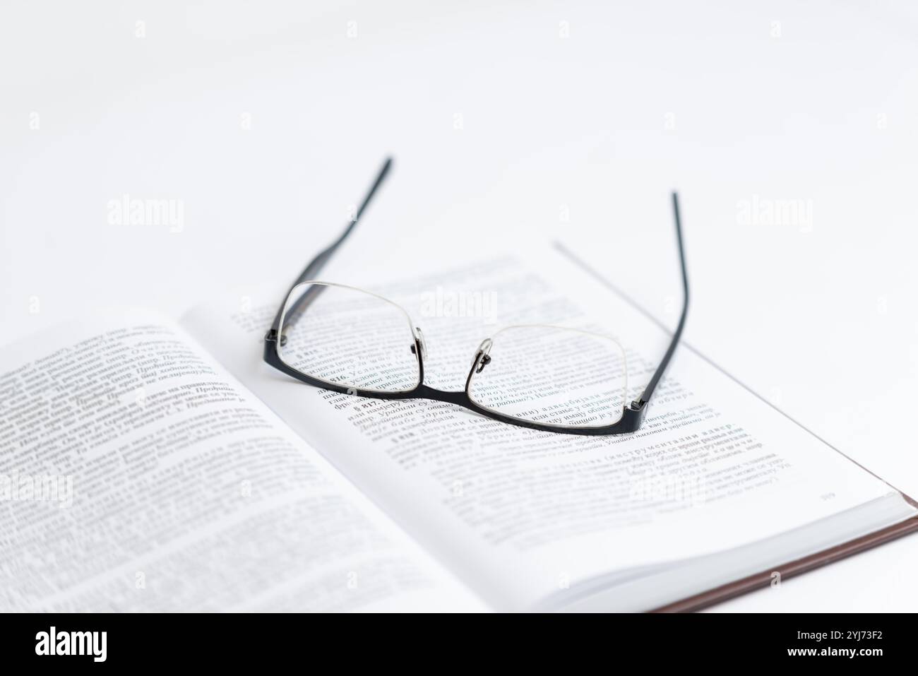 Brille auf offenem Buch mit Text, symbolisiert Lesen, Forschung, Wissenschaft und Rechtswissenschaft. repräsentiert die fokussierte Erforschung von Wissen und Akade Stockfoto