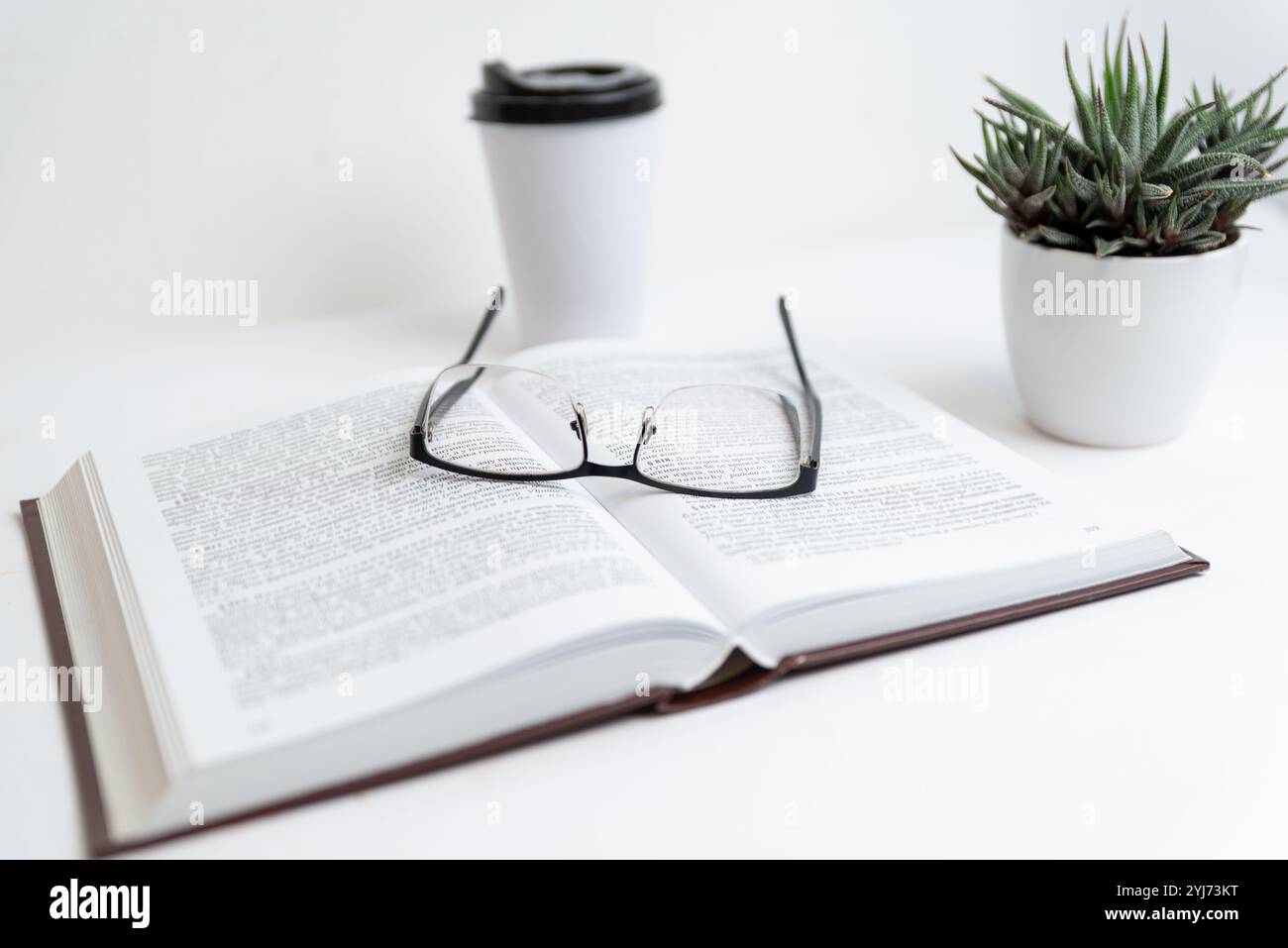 Gläser auf offenem Buch mit Kaffeetasse und Pflanze, symbolisiert entspanntes Lese- oder Lernumfeld, konzentriert sich auf Lernen, ruhige Atmosphäre Stockfoto