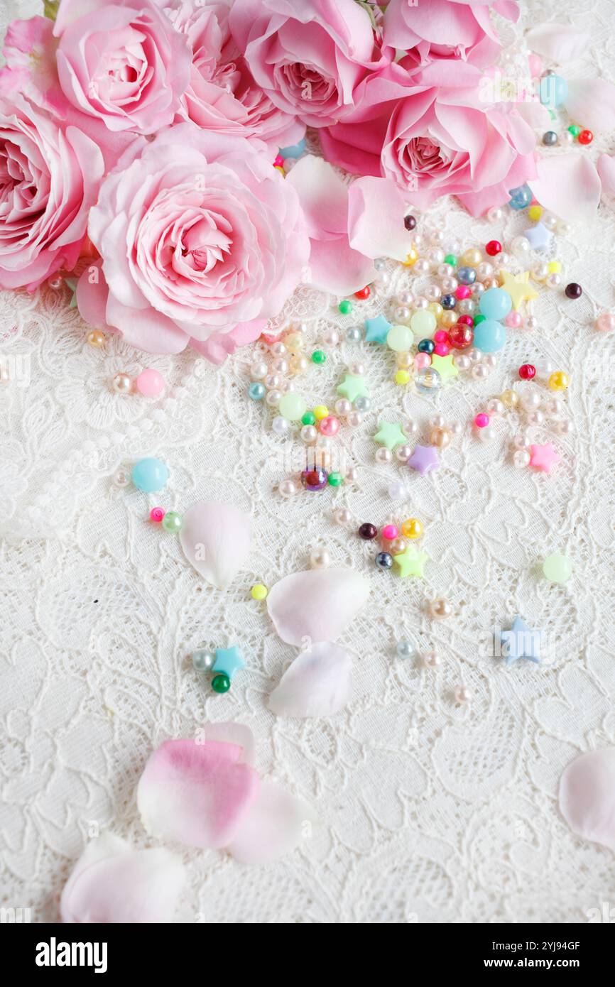 Rosafarbene Rosenblüte mit verstreuten Blütenblättern und bunten Perlen Stockfoto