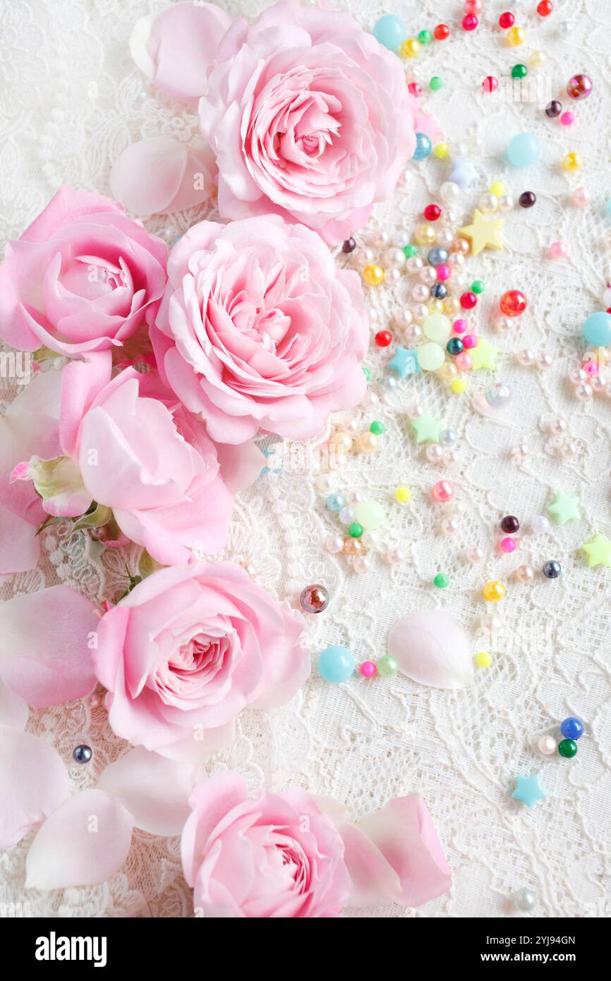 Rosafarbene Rosenblüte mit verstreuten Blütenblättern und bunten Perlen Stockfoto