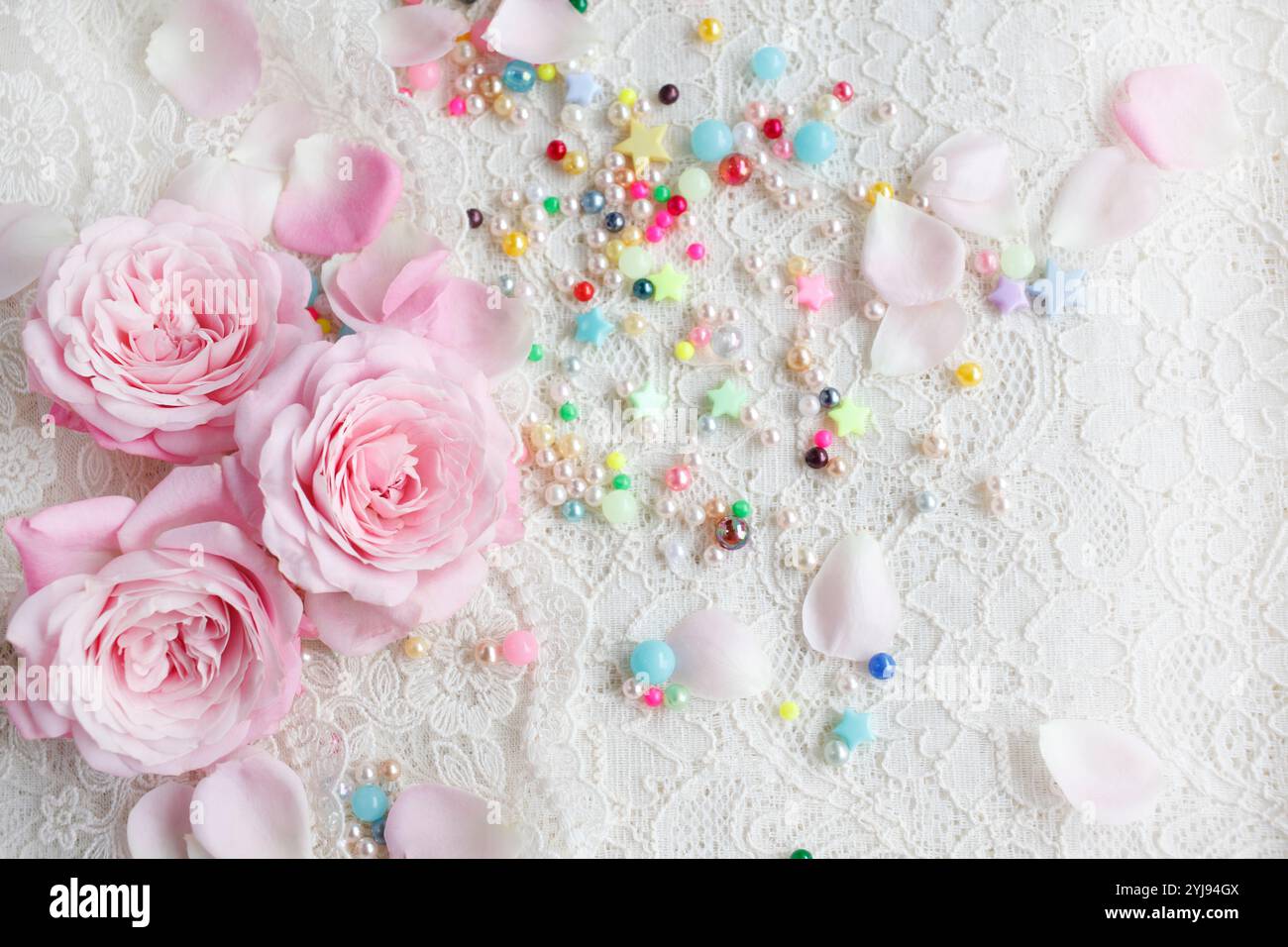Rosafarbene Rosenblüte mit verstreuten Blütenblättern und bunten Perlen Stockfoto
