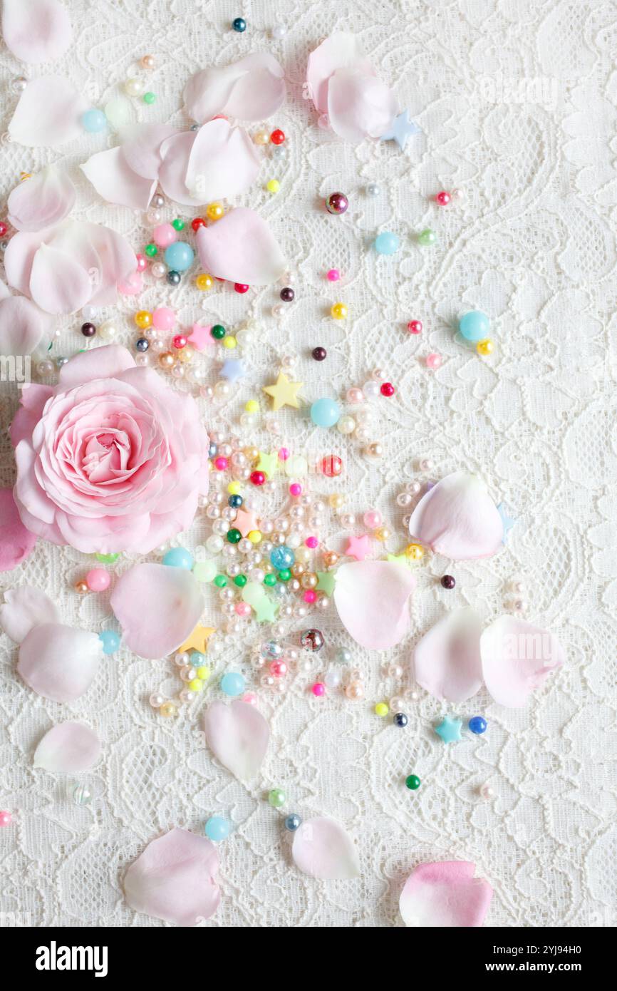 Rosafarbene Rosenblüte mit verstreuten Blütenblättern und bunten Perlen Stockfoto