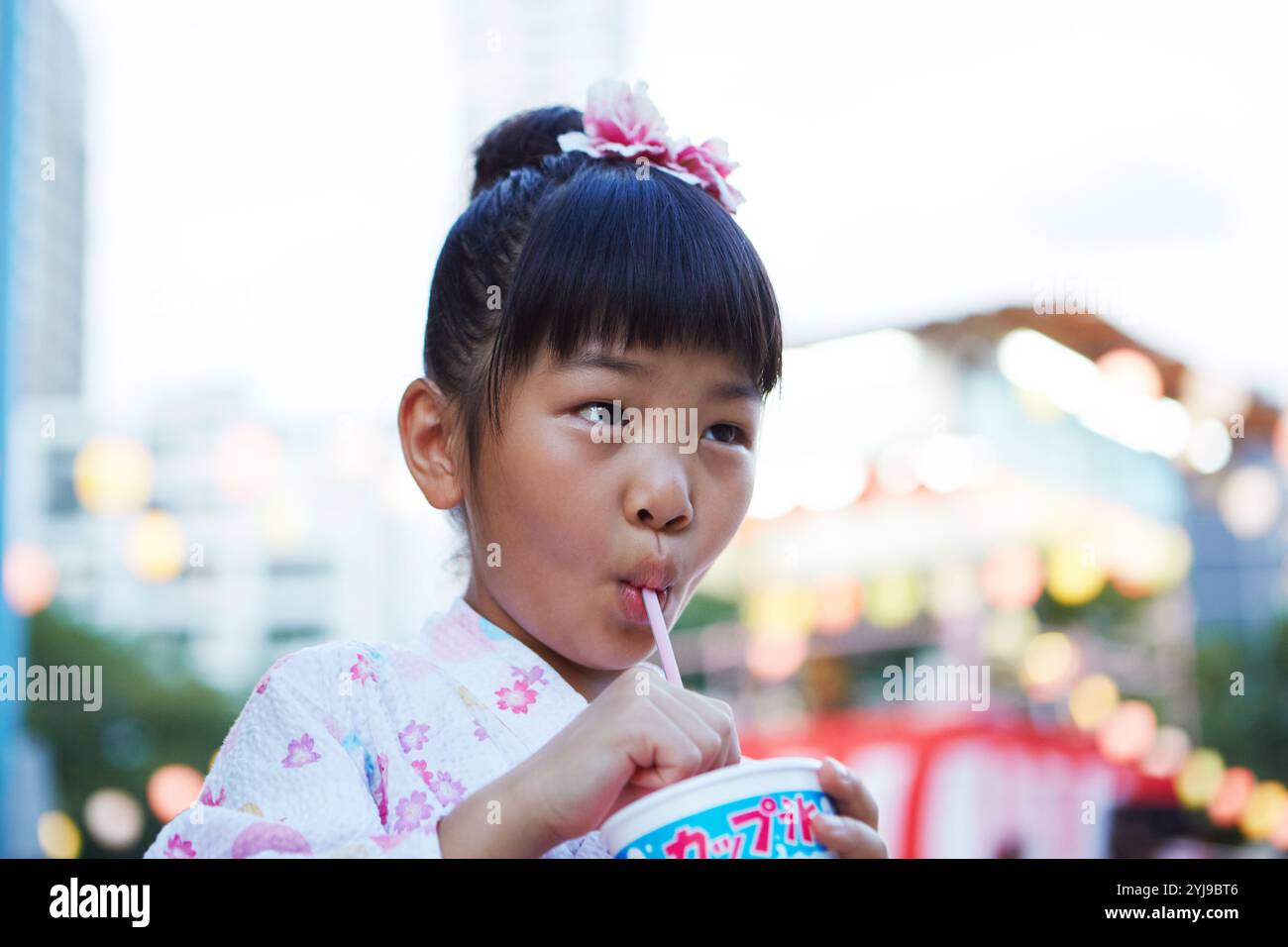 Ein Mädchen in Yukata trinkt geschmolzenes, rasiertes Eis durch einen Strohhalm Stockfoto