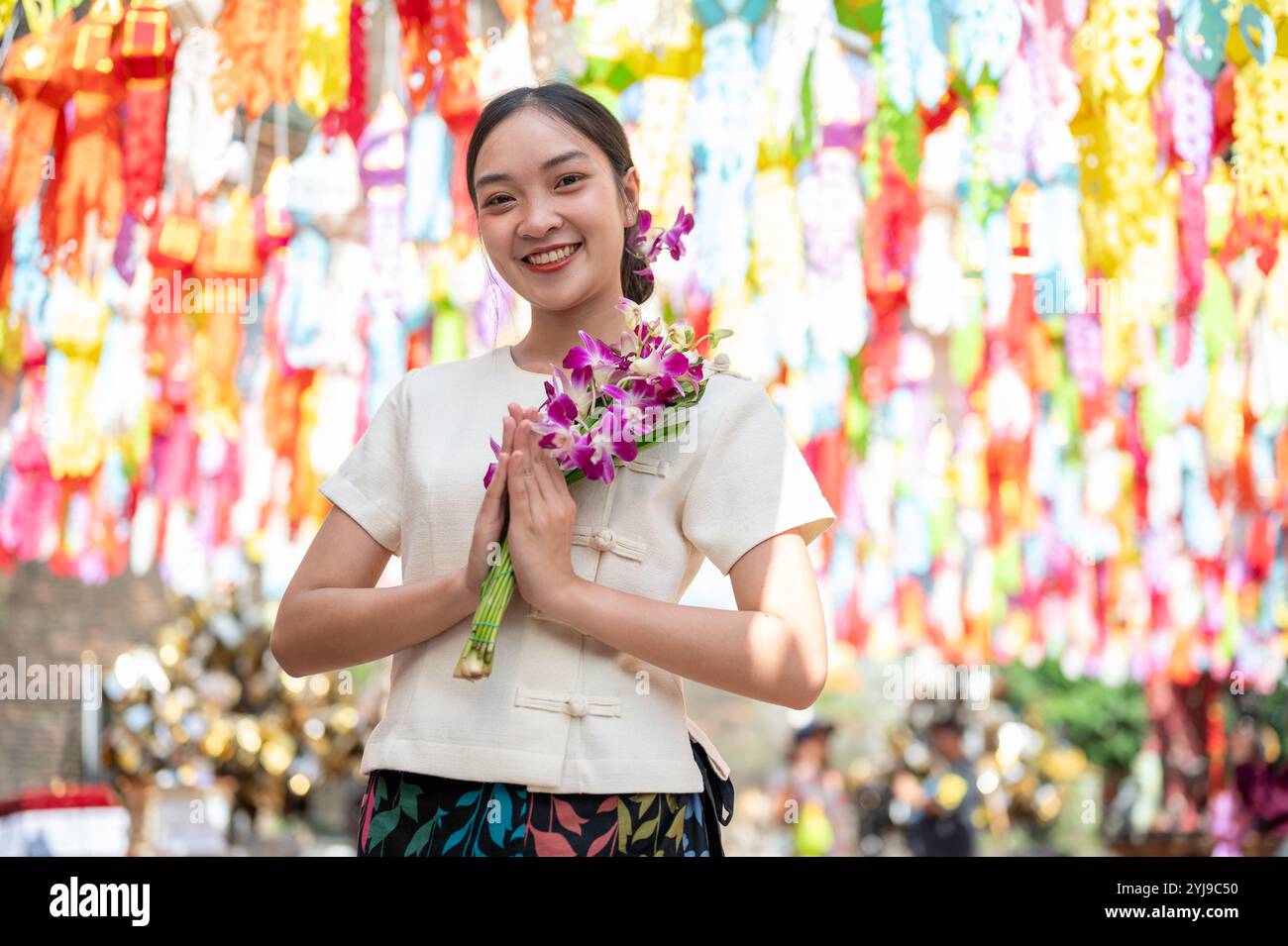 Eine charmante asiatische Frau in traditionellem nordischem Kleid steht in einem Tempel, lächelt in die Kamera und hält einen Blumenstrauß aus Orchideen mit farbenfroher Lanze Stockfoto
