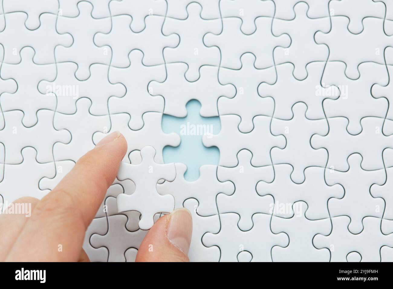 Die Hand hält eines der Teile eines leeren weißen Puzzles Stockfoto