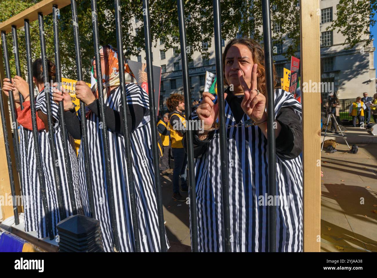 London, Großbritannien. Oktober 2018. Frauen in Prionenkleidung stehen hinter Gefängnisgittern beim Protest. Hinter dem Banner "Demokratie im Iran mit Maryam Rajavi" protestierten die iranischen Volksmudschaheddin gegen das repressive gegenwärtige Regime im Iran, mit einem Gibbet und drei Frauen in einer Gefängniszelle, die die Herrschaft des Terrors dort illustrieren und ein Ende der Hinrichtungen dort forderten. Plakate erinnerten uns daran, dass das iranische Regime der Weltrekordhalter für Hinrichtungen ist. Rajavi, der Vorsitzende der PMOI, hat ein 10-Punkte-Manifest vorgelegt, in dem ein modernes Rechtssystem, die Gleichstellung der Geschlechter und das politische usw. gefordert werden Stockfoto