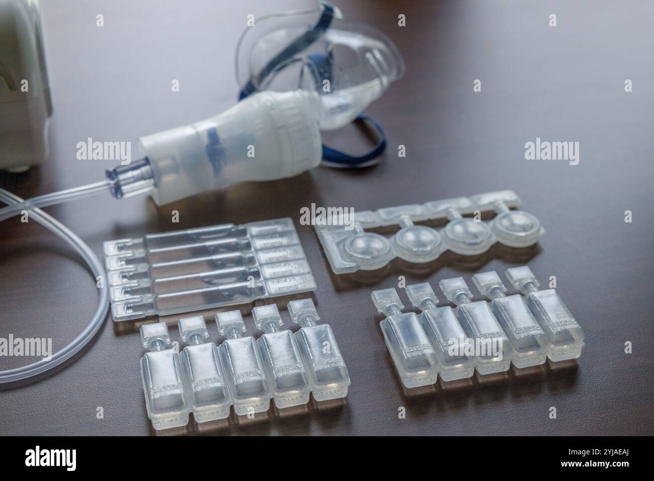 Eine Vielzahl von kleinen medizinischen Ampullen und Fläschchen, die für die Inhalationstherapie verwendet werden, auf einem Tisch mit einem Vernebler im Hintergrund angeordnet Stockfoto