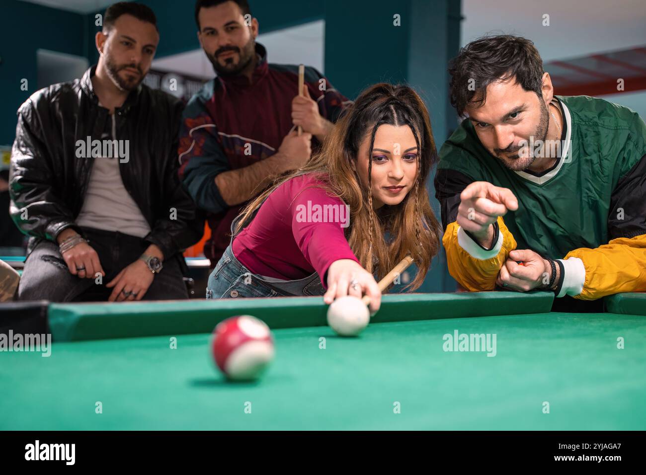 Frau demonstrierte Schwimmbadschießtechnik, während drei Freunde während des freundlichen Billardspiels in der örtlichen Sportbar beobachten und trainieren Stockfoto