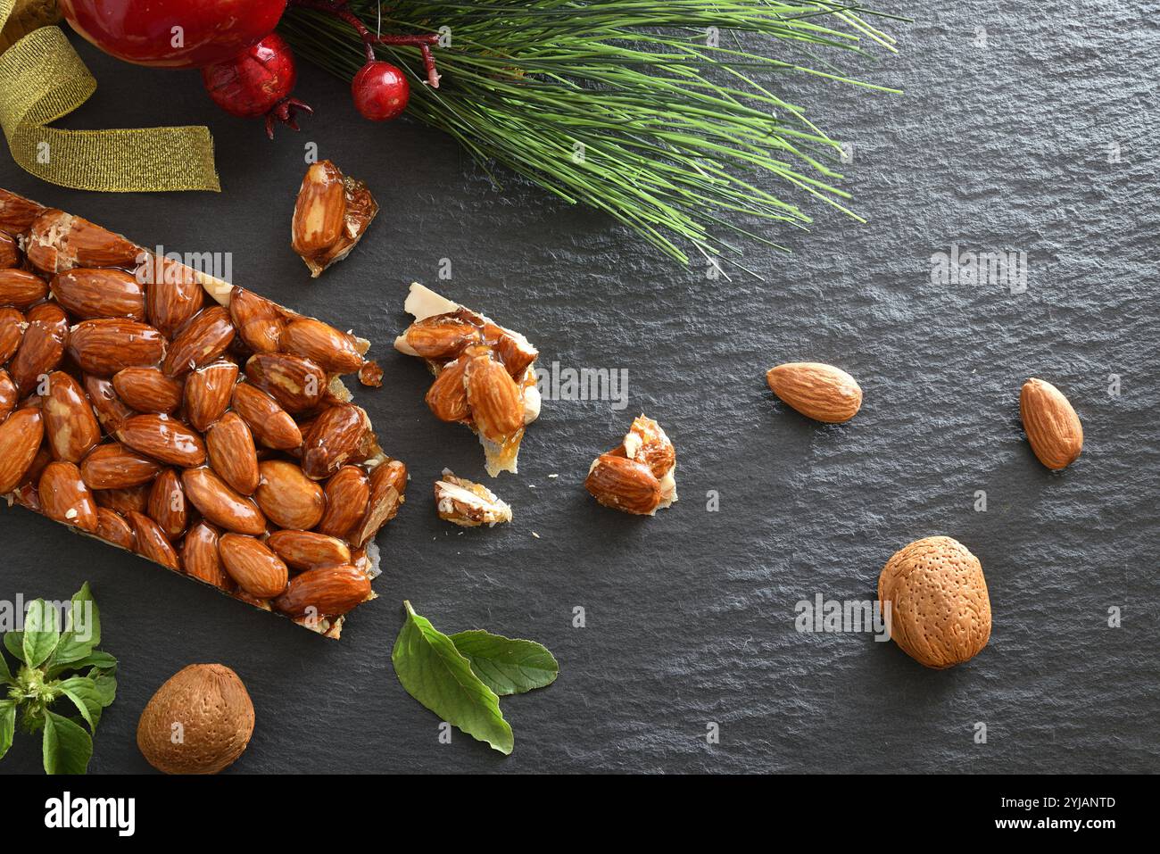 Harter Nougat mit ganzen und gehackten Mandeln auf einem Schieferteller mit natürlichen Mandeln und Weihnachtsdekoration. Draufsicht. Stockfoto