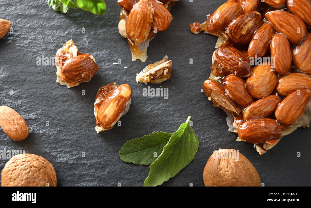 Harter Nougat mit ganzen und gehackten Mandeln auf einem Schieferteller mit natürlichen Mandeln und Blättern aus nächster Nähe. Draufsicht. Stockfoto