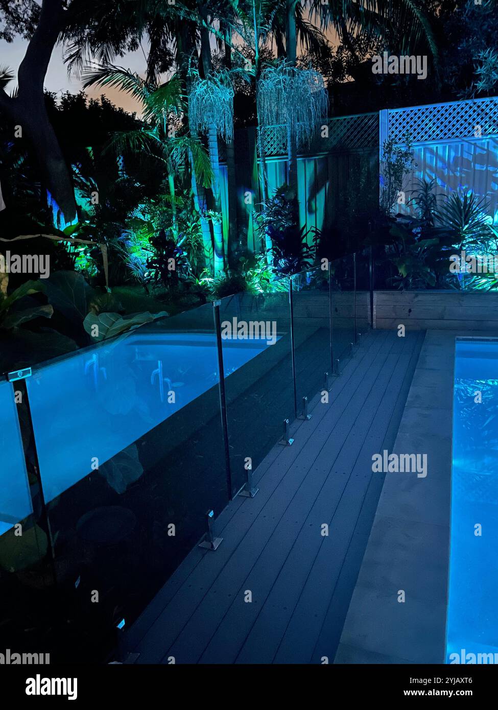 Außenpool aus Beton mit Reflexen im Wasser. Blaue und grüne Lichter im Garten bei Nacht im Hinterhof von Australien mit Glaszaun. Stockfoto