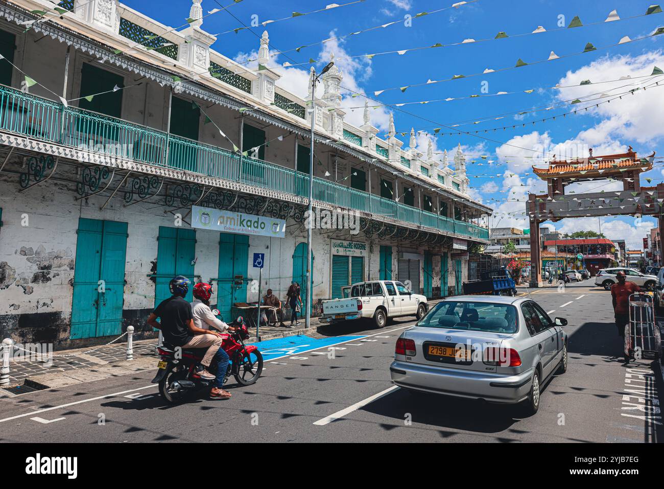 Ein Mann fährt selbstbewusst mit seinem Motorrad eine Straße in Port Louis City entlang, vorbei an einem Auto. Stockfoto