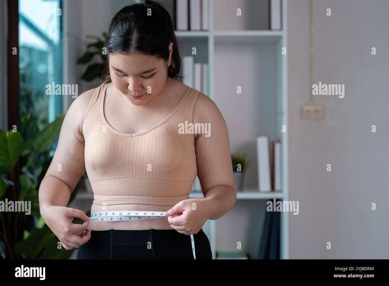 Frau, die Taille mit Bandmaß im modernen Innenraum für Fitness und Gesundheit Lifestyle Konzept misst Stockfoto