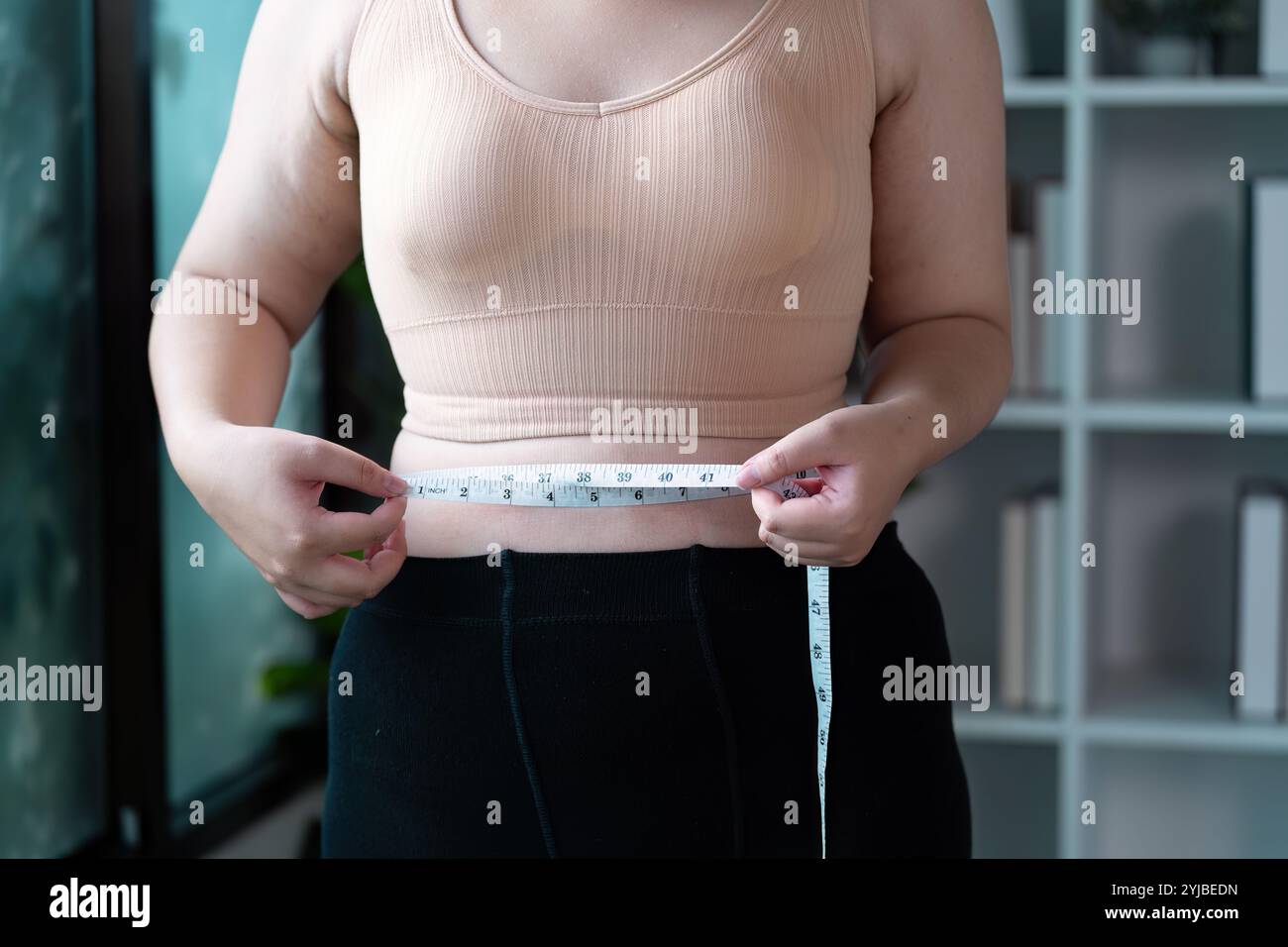 Woman Measuring Taille mit Tape Measure in modernen Home Setting for Fitness and Health Tracking Stockfoto