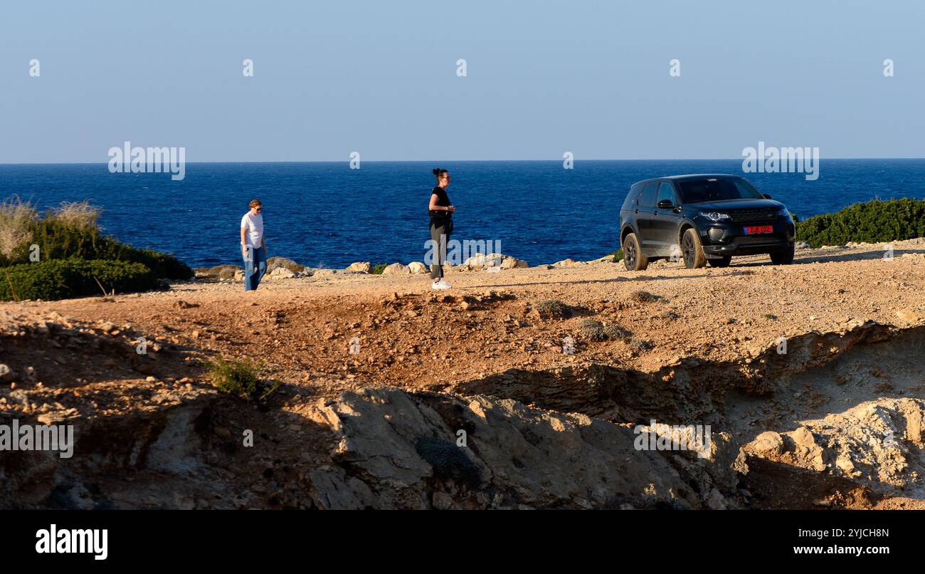 Zwei Personen spazieren durch ein felsiges Gelände und genießen an einem sonnigen Tag den atemberaubenden Blick aufs Meer. Stockfoto