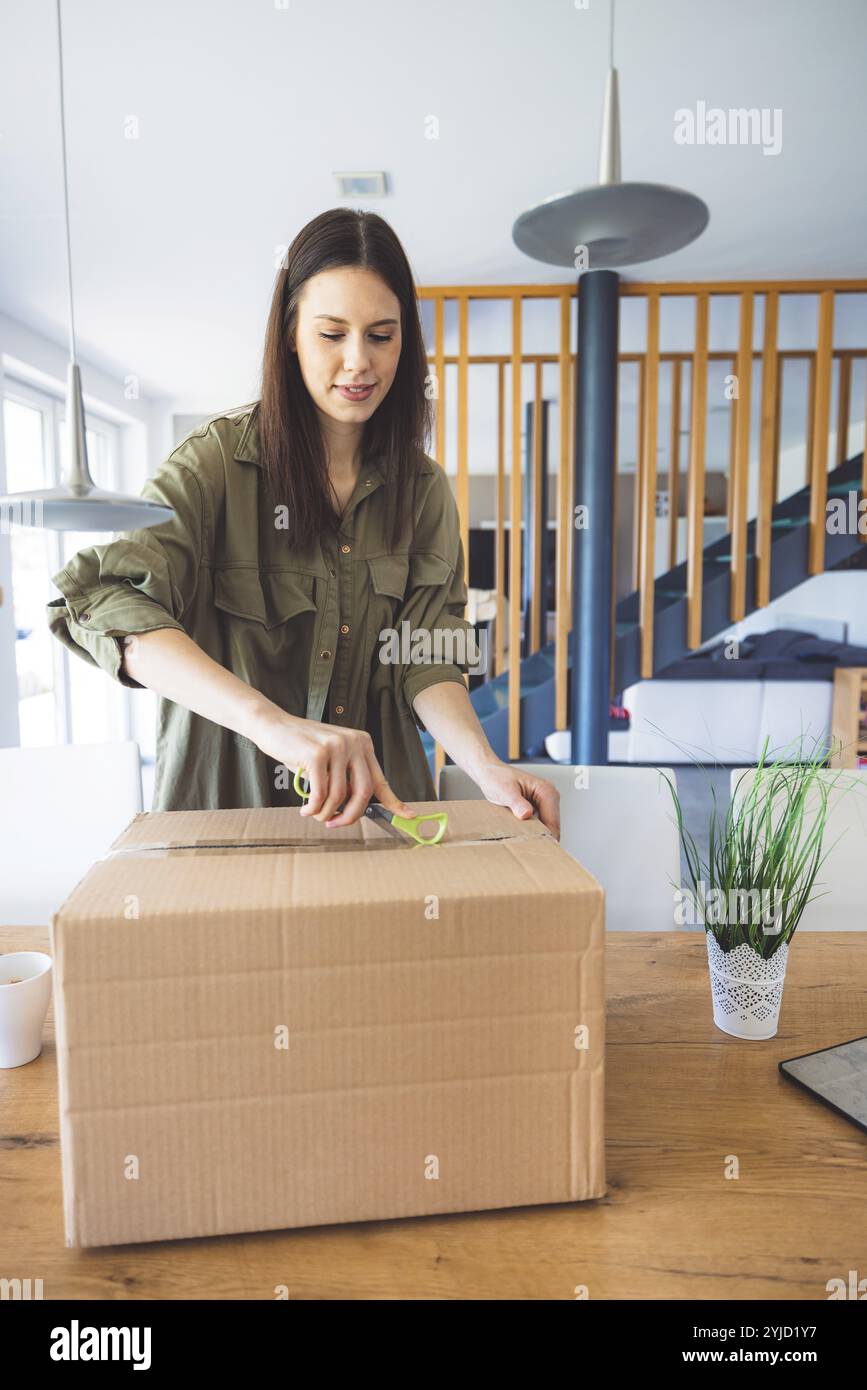 Junge kaukasische Frau erhält eine große Kiste mit ihren Online-Bestellungen. Frau, die das Paket öffnet und begeistert ist, das Zeug zu sehen, das sie gekauft hat. Stockfoto