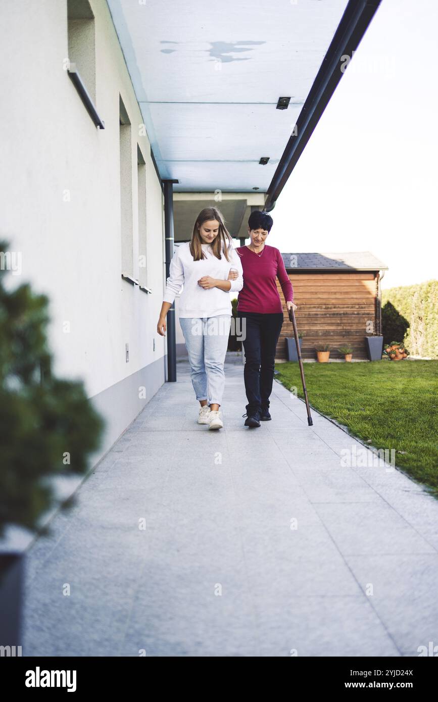 Junge kaukasische Frau, Krankenschwester, bei einem Hausbesuch, um eine Seniorin zu versorgen. Die Schwester hilft einer Seniorin bei den täglichen Aufgaben, hilft ihr, zu laufen Stockfoto