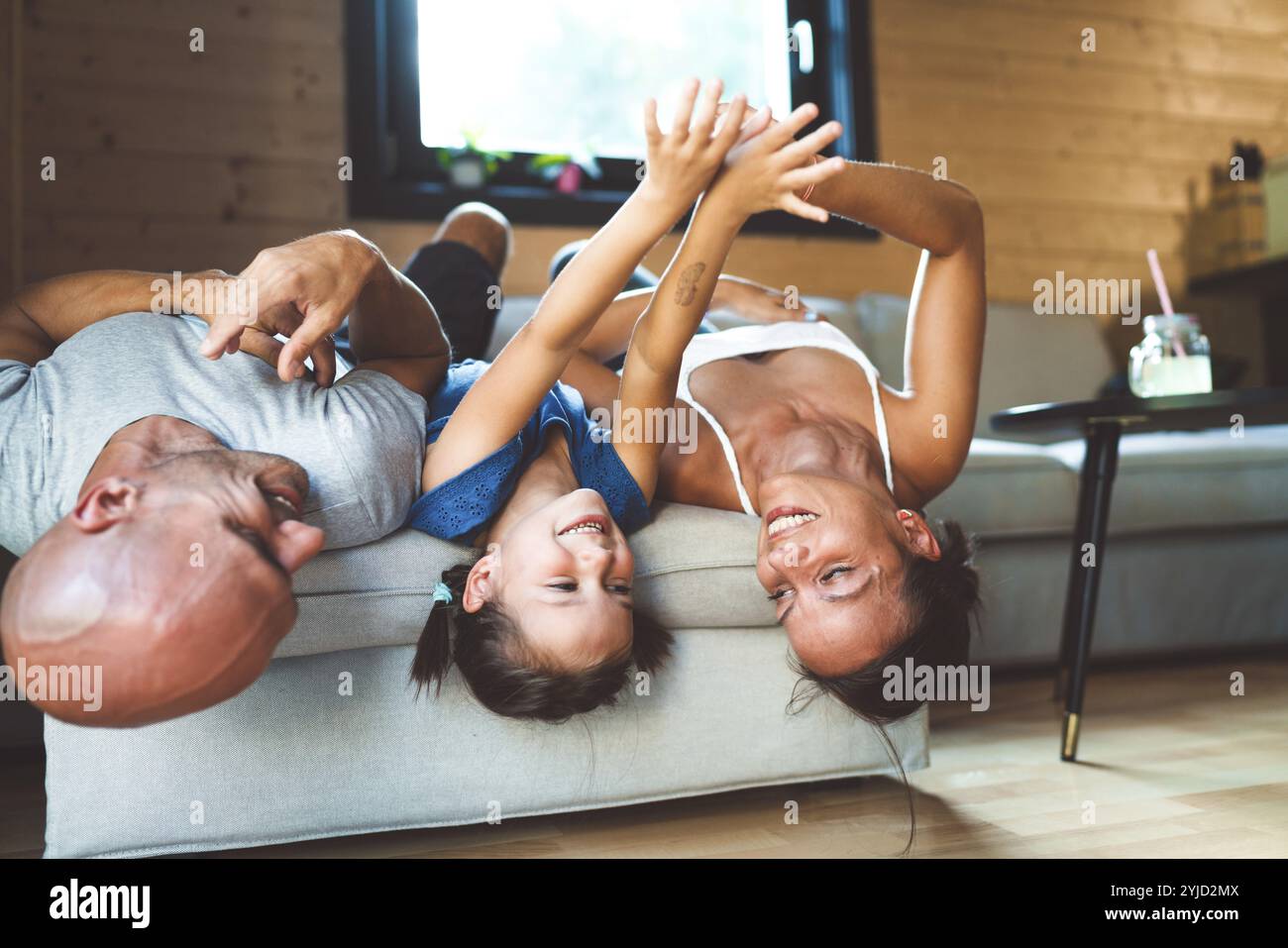 Eine junge Familie mit einem Mädchen, die am Wochenende zu Hause ist. Liebevolle Familie, die sich auf der Couch ausruht, spielt, Fernsehen sieht Stockfoto