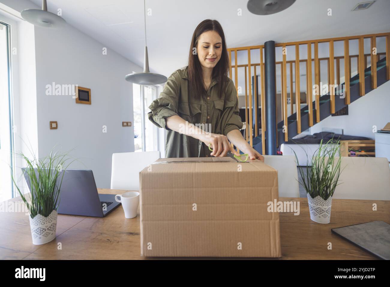 Junge kaukasische Frau erhält eine große Kiste mit ihren Online-Bestellungen. Frau, die das Paket öffnet und begeistert ist, das Zeug zu sehen, das sie gekauft hat. Stockfoto