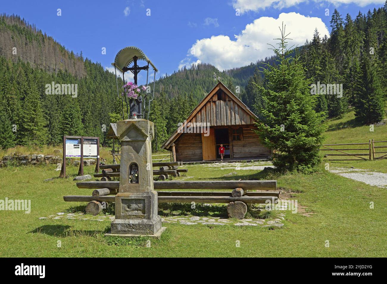 Kreuz und Holzhütte in der Huciska-Lichtung im Chocholowska-Tal. Die Berghänge sind mit Fichtenwald bedeckt Stockfoto