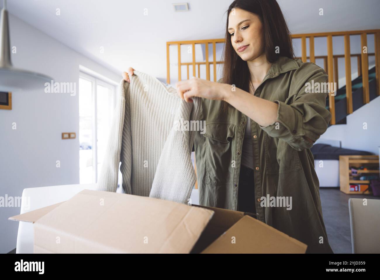Junge kaukasische Frau erhält eine große Kiste mit ihren Online-Bestellungen. Frau, die das Paket öffnet und begeistert ist, das Zeug zu sehen, das sie gekauft hat. Stockfoto
