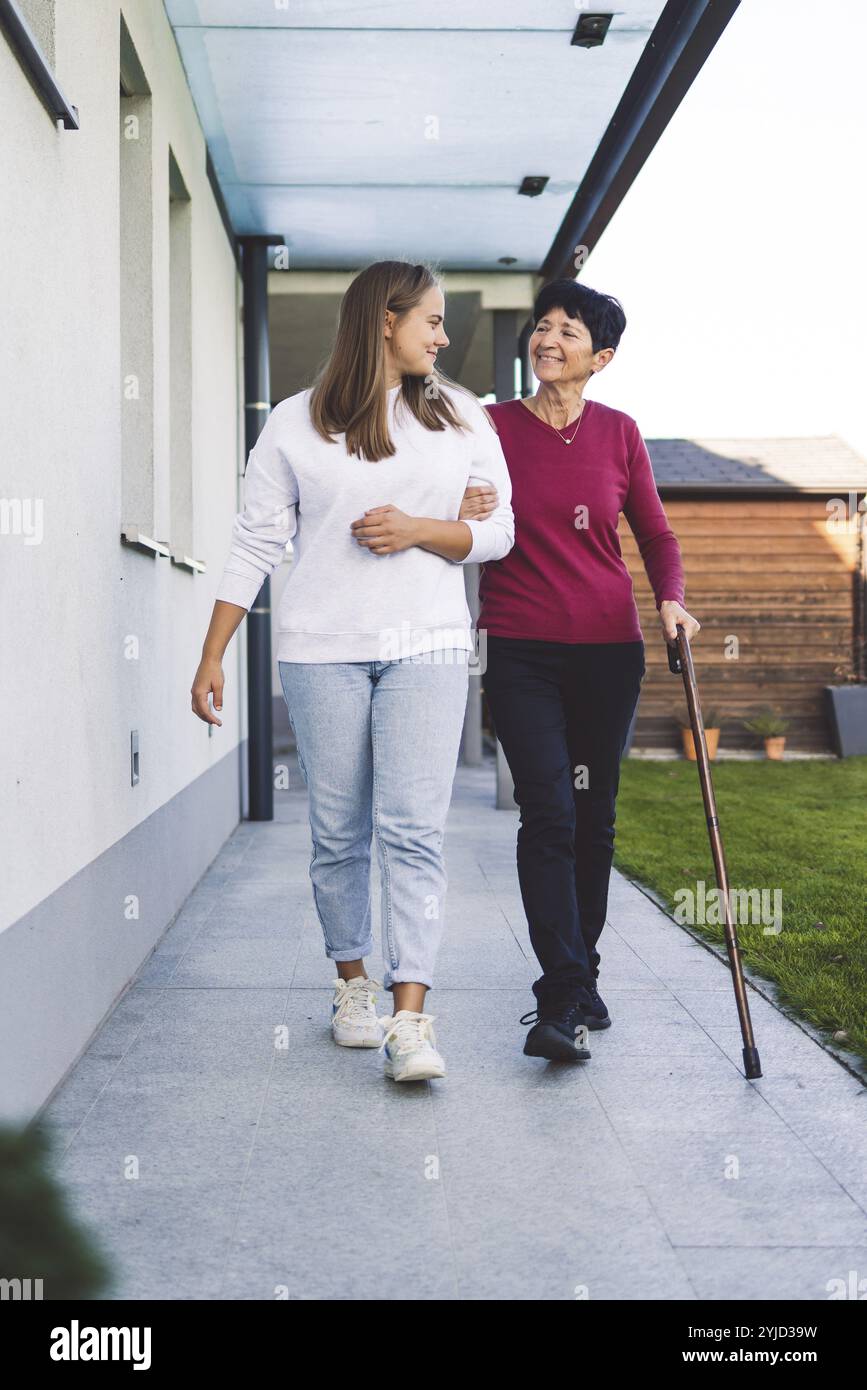 Junge kaukasische Frau, Krankenschwester, bei einem Hausbesuch, um eine Seniorin zu versorgen. Die Schwester hilft einer Seniorin bei den täglichen Aufgaben, hilft ihr, zu laufen Stockfoto