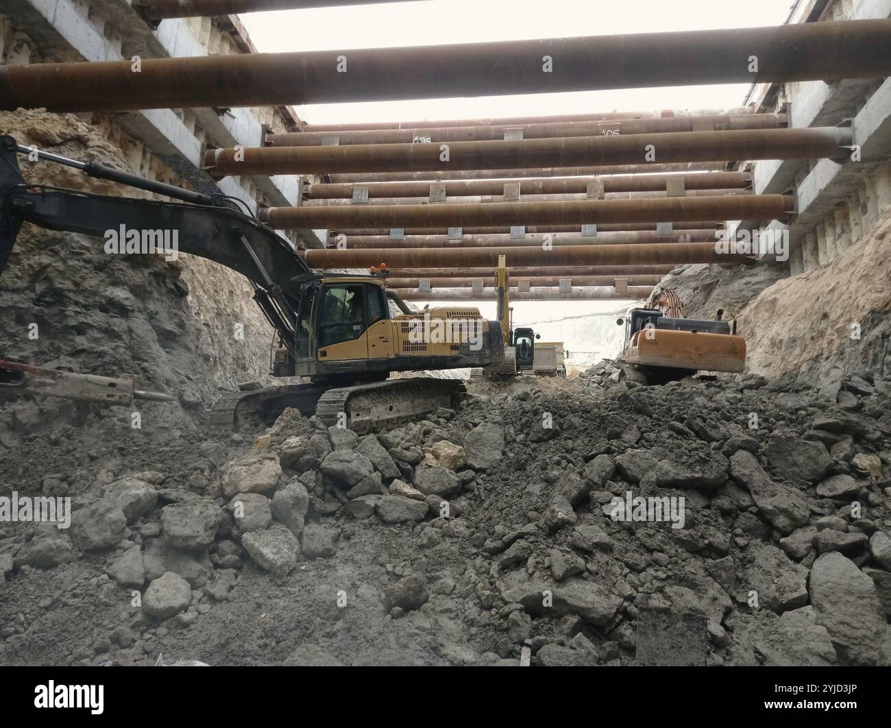 Baustelle mit einem Bagger, der Steine und Schutt bewegt, verstärkt durch Stahlträger Stockfoto