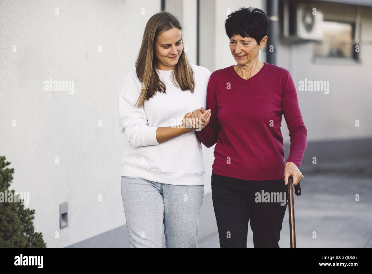 Junge kaukasische Frau, Krankenschwester, bei einem Hausbesuch, um eine Seniorin zu versorgen. Die Schwester hilft einer Seniorin bei den täglichen Aufgaben, hilft ihr, zu laufen Stockfoto