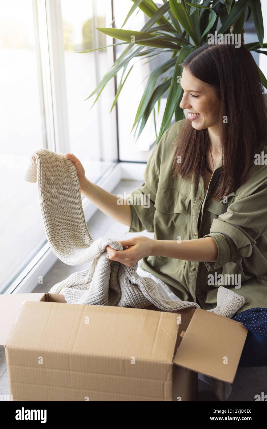 Junge kaukasische Frau erhält eine große Kiste mit ihren Online-Bestellungen. Frau, die das Paket öffnet und begeistert ist, das Zeug zu sehen, das sie gekauft hat. Stockfoto